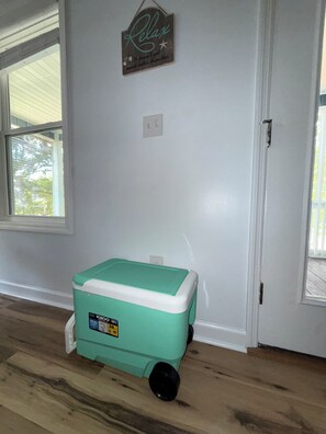 A room with a teal and white cooler, a wall sign that says 'Relax,' and a window. - Family & Dog Friendly Retreat w. Beach, Dog, and Baby Gear. Screened porch! (Oak Island)