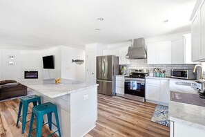 A modern kitchen with white cabinets, stainless steel appliances, and a marble island. - Family & Dog Friendly Retreat w. Beach, Dog, and Baby Gear. Screened porch! (Oak Island)