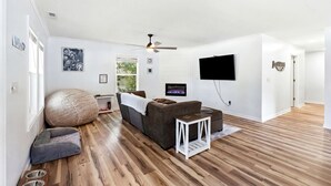 Un soggiorno moderno con un divano, un pouf e una poltrona sacco, una televisione a schermo piatto montata a parete e una ventola a soffitto.