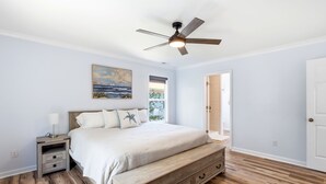 Una camera da letto con un letto, un comodino, una cassettiera, una ventola a soffitto e un quadro appeso al muro.