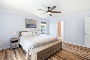 A bedroom with a bed, nightstand, dresser, ceiling fan, and a painting on the wall. - Family & Dog Friendly Retreat w. Beach, Dog, and Baby Gear. Screened porch! (Oak Island)