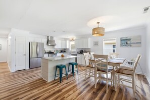 A modern kitchen with white cabinets, a stainless steel refrigerator, and a wooden island with stools. - Family & Dog Friendly Retreat w. Beach, Dog, and Baby Gear. Screened porch! (Oak Island)