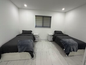 A room with two beds, a window with blinds, white walls, and a marble-patterned floor. - Modern unit with premium finish, porcelain floor and rain fall shower (Hollywood)