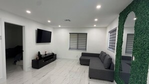 A modern living room with a flat-screen TV, grey sofa, and a decorative green wall. - Modern unit with premium finish, porcelain floor and rain fall shower (Hollywood)
