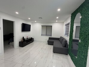Ein modernes Wohnzimmer mit Flachbildfernseher, grauem Sofa und einer dekorativen grünen Wand.