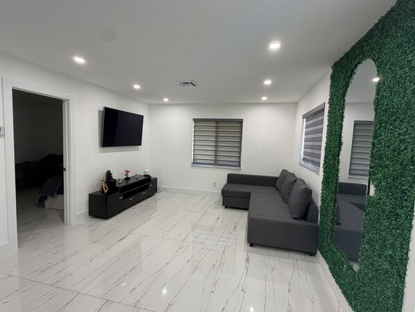A modern living room with a flat-screen TV, grey sofa, and a decorative green wall. - Modern unit with premium finish, porcelain floor and rain fall shower (Hollywood)