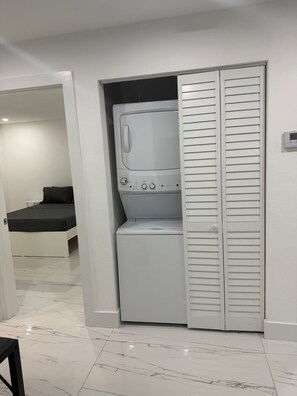 Ein kleiner Waschraum mit Waschmaschine und Trockner, eine Sitzecke mit einer Bank und eine Tür zu einem weiteren Raum.