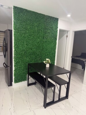 A room with a green wall, a black table with a vase, and a bed in the background. - Modern unit with premium finish, porcelain floor and rain fall shower (Hollywood)