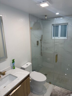 A modern bathroom with a glass-enclosed shower, a white toilet, and a marble countertop sink. - Modern unit with premium finish, porcelain floor and rain fall shower (Hollywood)