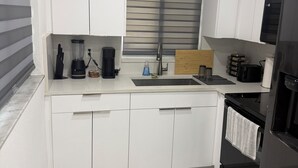 A modern kitchen with white cabinets, a black refrigerator, and a marble floor. - Modern unit with premium finish, porcelain floor and rain fall shower (Hollywood)