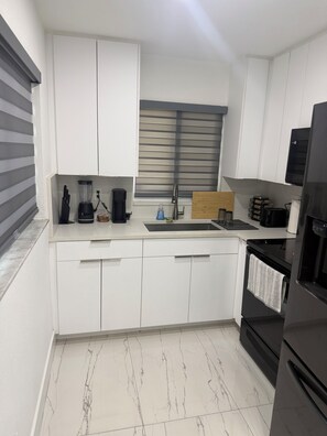 Eine moderne Küche mit weißen Schränken, einem schwarzen Kühlschrank und einem Marmorboden.