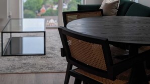Un salon moderne avec une table ronde, deux chaises, un canapé, une lampe sur pied et une grande fenêtre donnant sur la ville.
