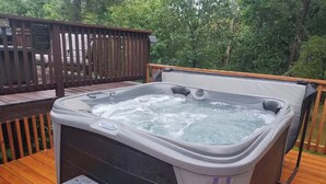 Een hottub op een houten terras, met een veiligheidsteken, omringd door bomen.