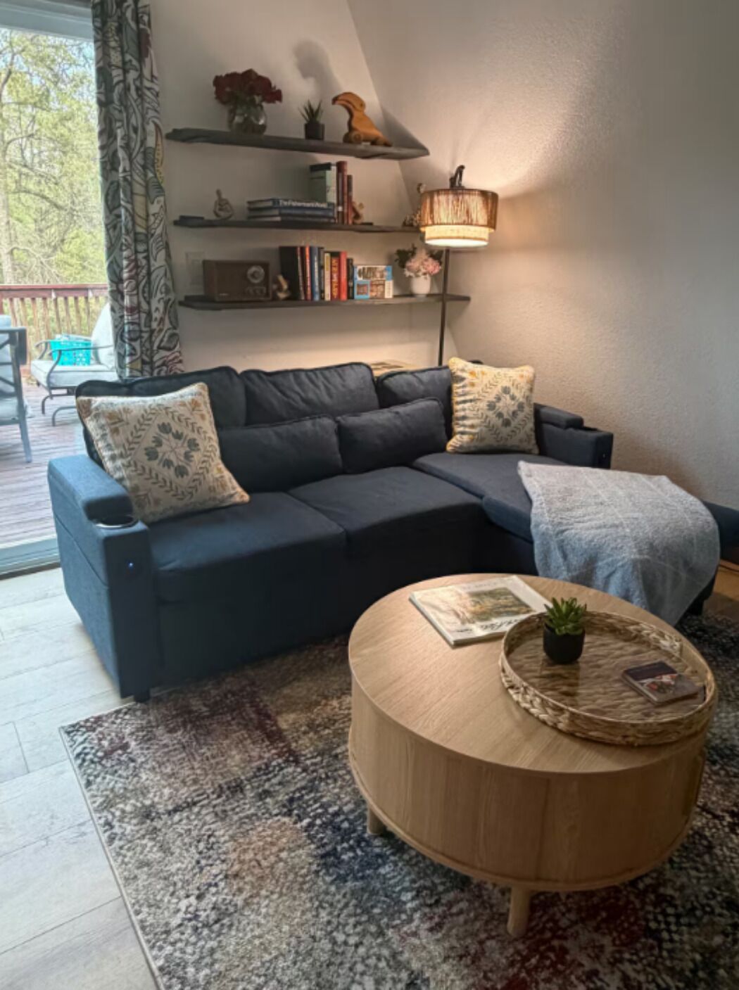 Ein modernes Wohnzimmer mit einem dunkelgrauen Ecksofa, einem runden Couchtisch aus Holz und einem Bücherregal mit Dekorationselementen.