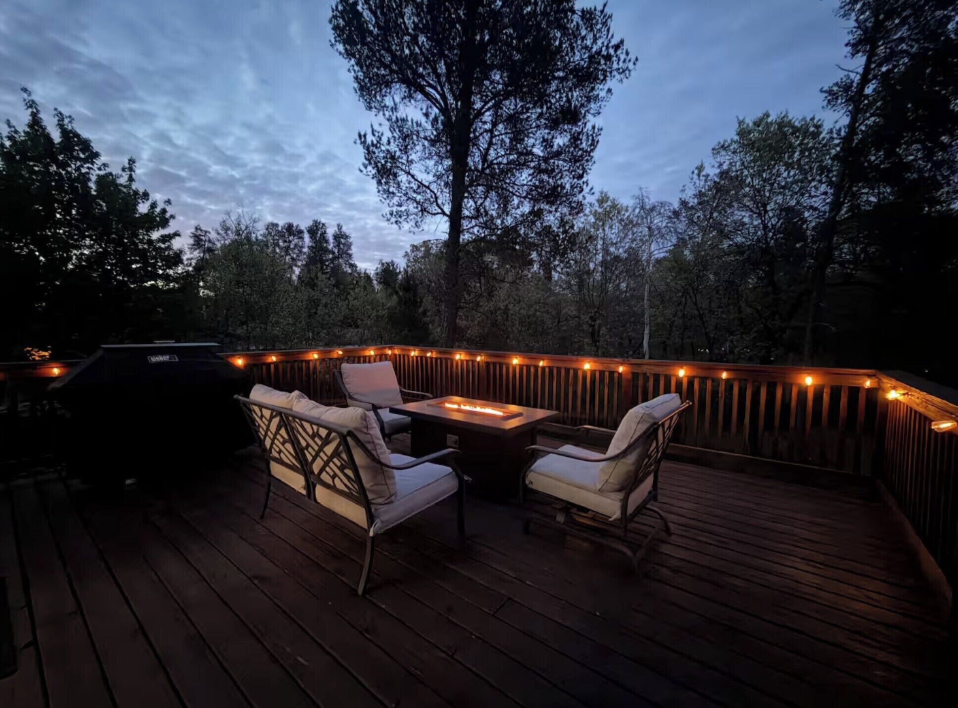 An outdoor deck with a fire feature, two chairs, and a grill.