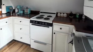 A compact kitchen with a white stove, white cabinets, and a wooden countertop.