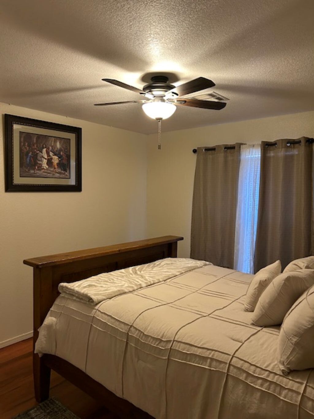 A bedroom with a bed, a ceiling fan, a window with curtains, and a framed picture on the wall.