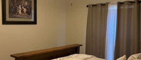 A bedroom with a bed, a ceiling fan, a window with curtains, and a framed picture on the wall.