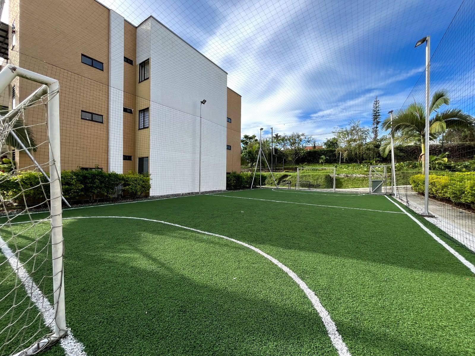 Un camp de futbol amb porteres, envoltat d'un edifici amb façana de disseny de rejola i un cel serè.