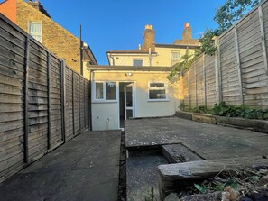 A narrow alleyway with a small house at the end, wooden fences on both sides, and a clear blue sky. - Fullhouse - Croydon centre (Croydon)