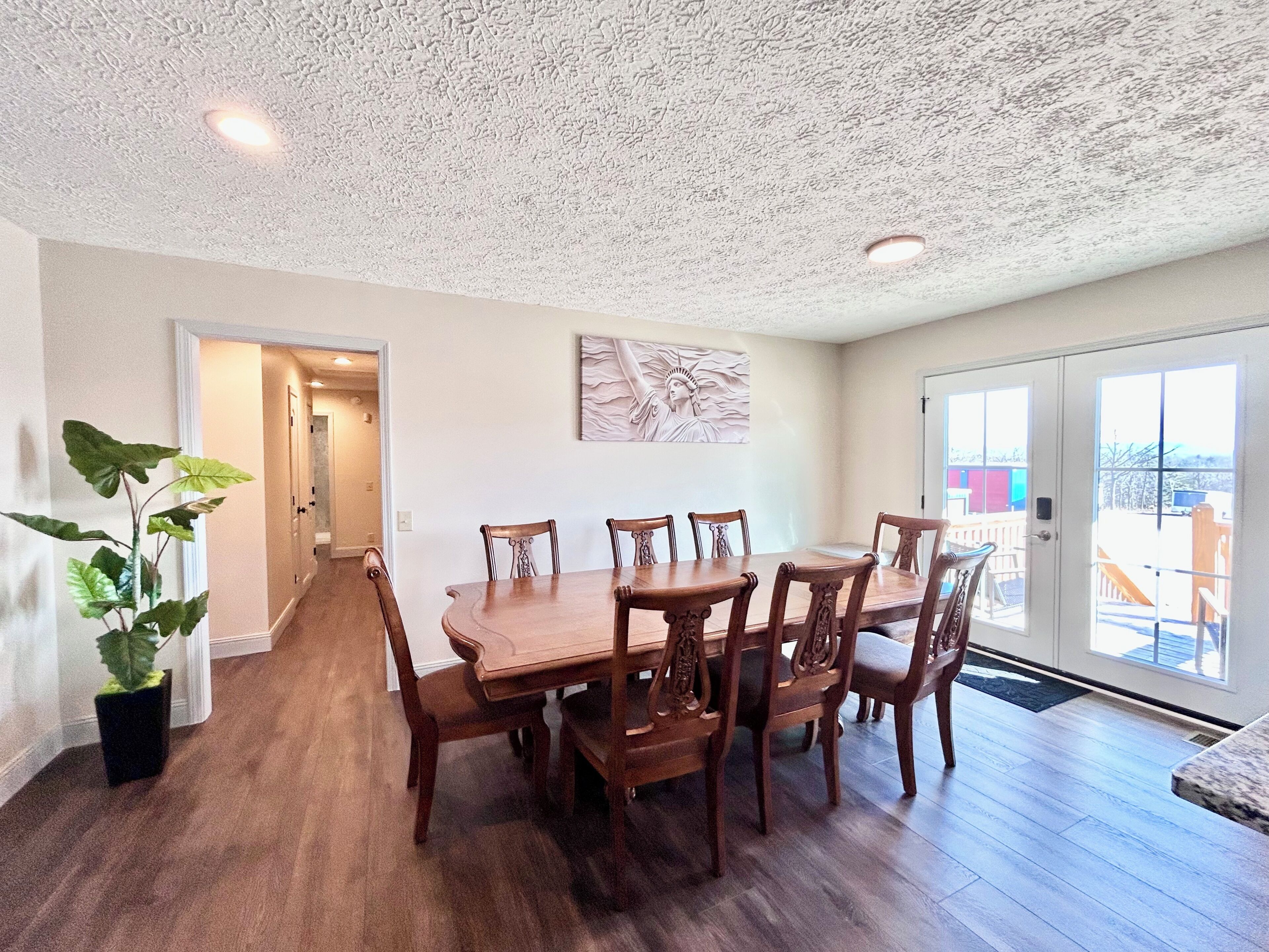 A dining area with a wooden table and chairs, a ceiling with textured plaster, and a view through a glass door.