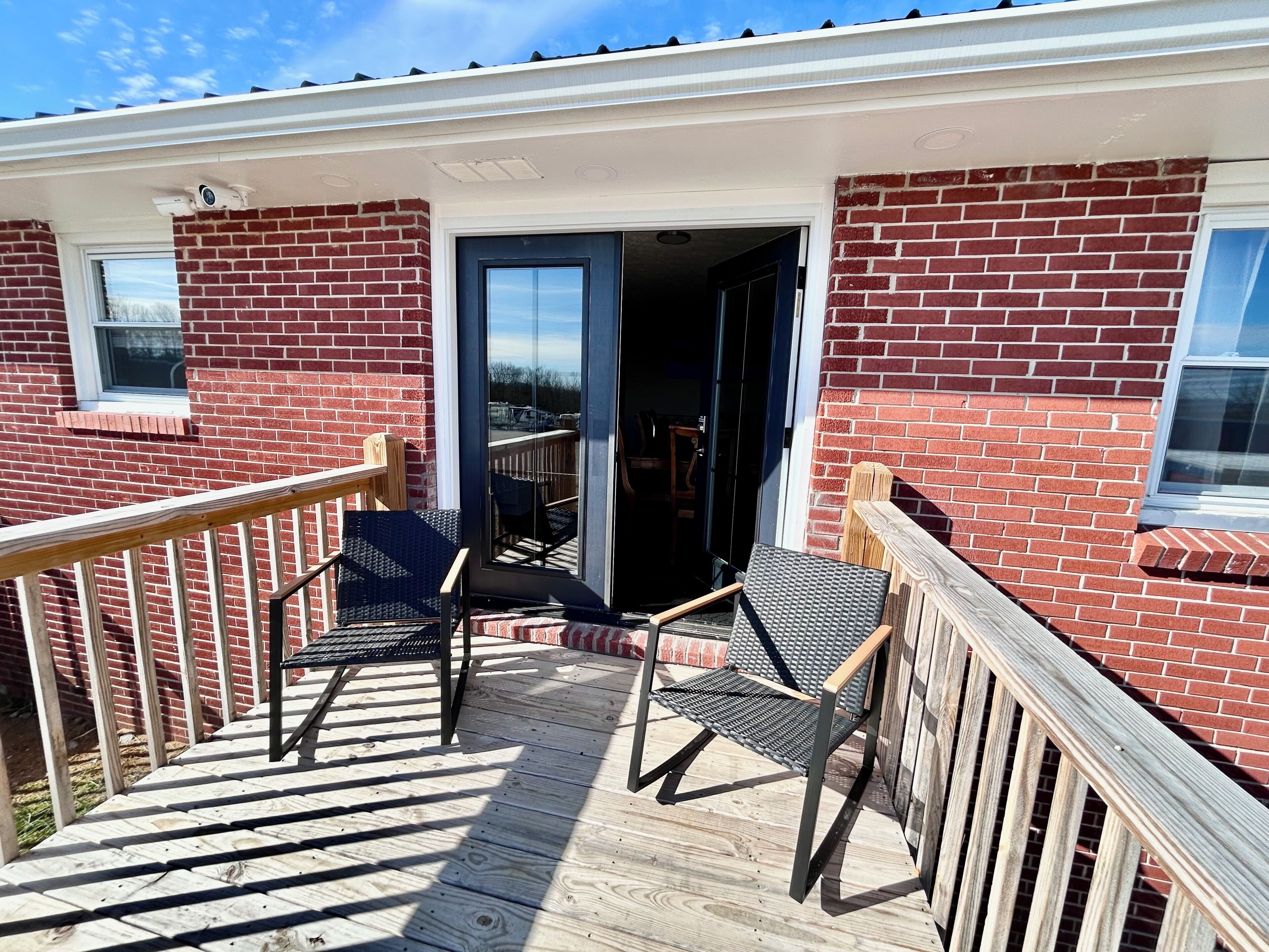 A covered deck with two chairs and a wooden railing.