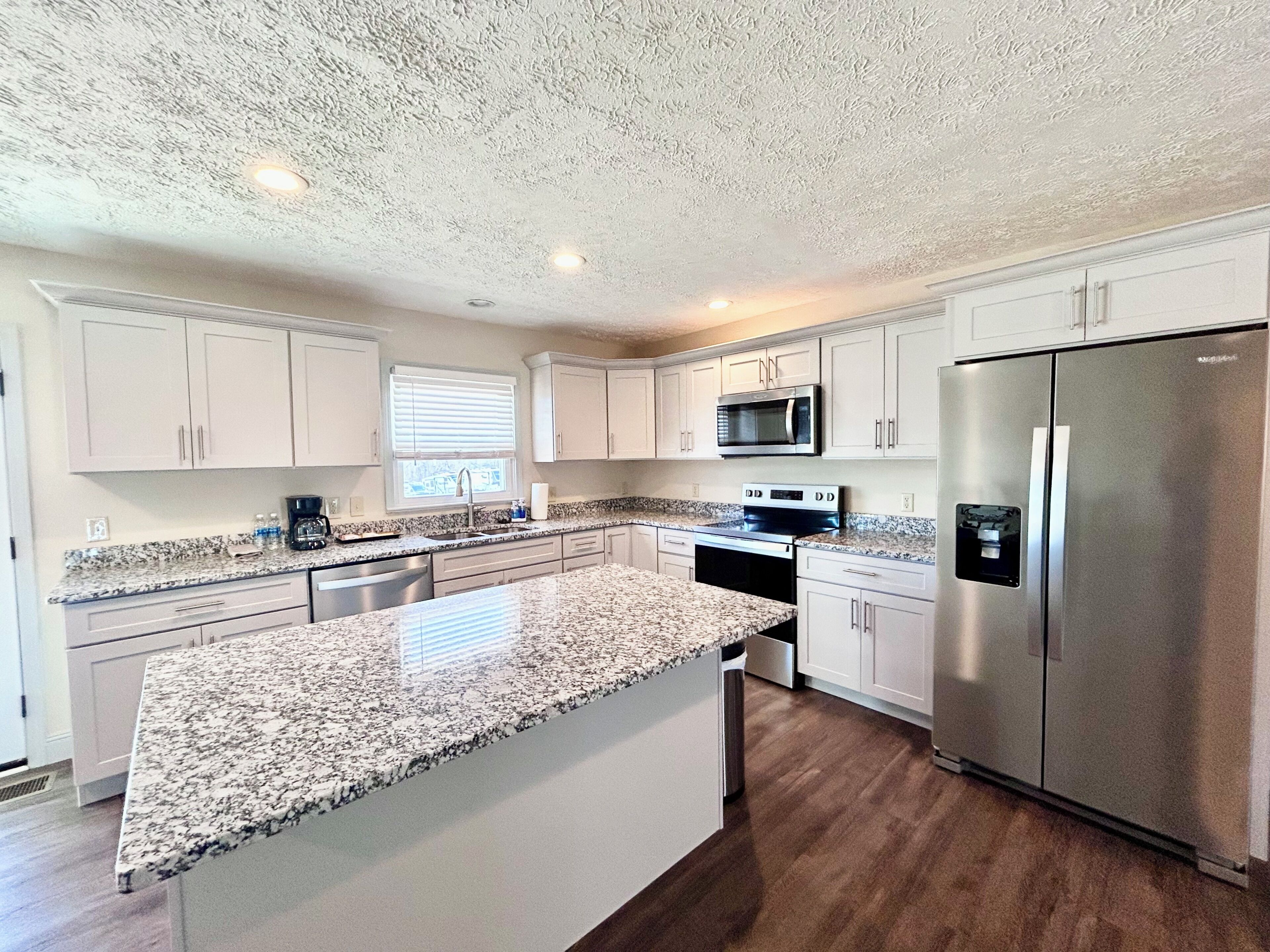 A modern kitchen with white cabinets, granite countertops, stainless steel appliances, and a central island.