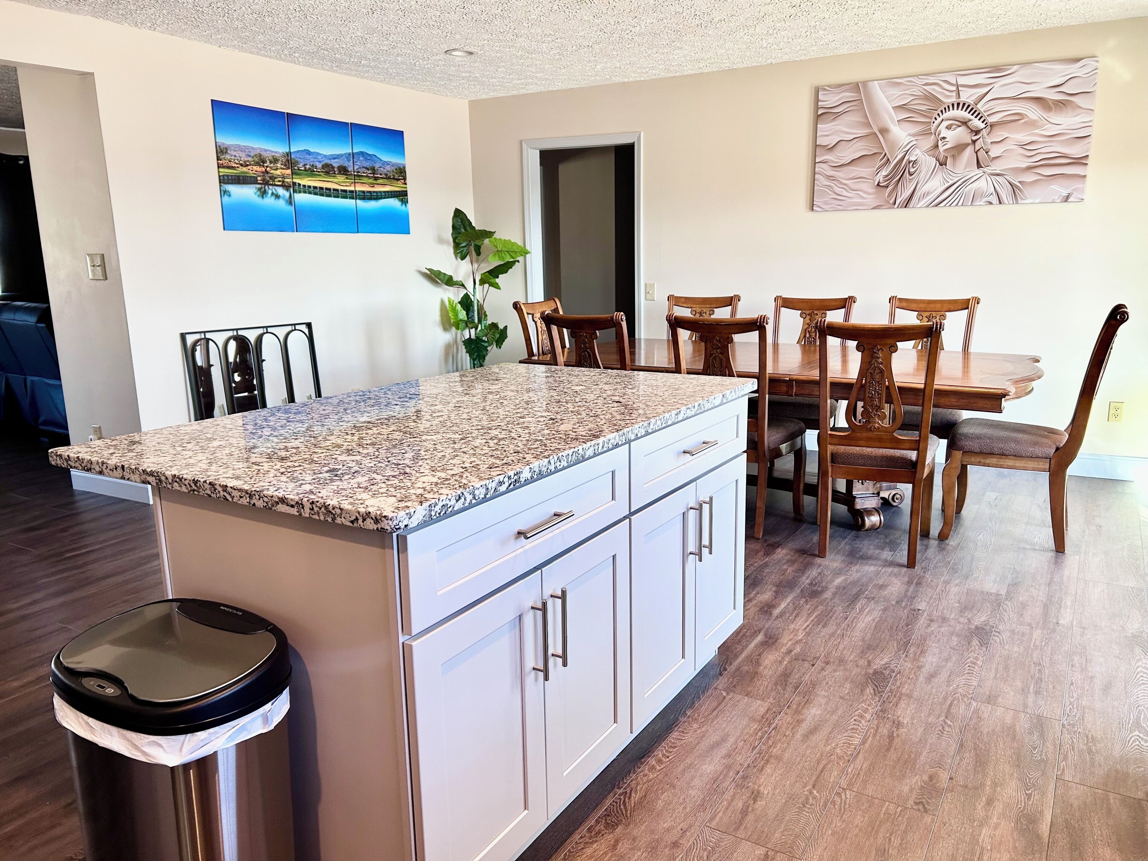 A kitchen with a granite countertop, white cabinets, and a trash can.