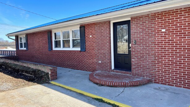 A red brick house with a black front door, white window frames, and a blue roof.