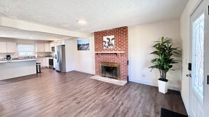 A spacious living area with a fireplace, hardwood flooring, and a kitchen in the background.