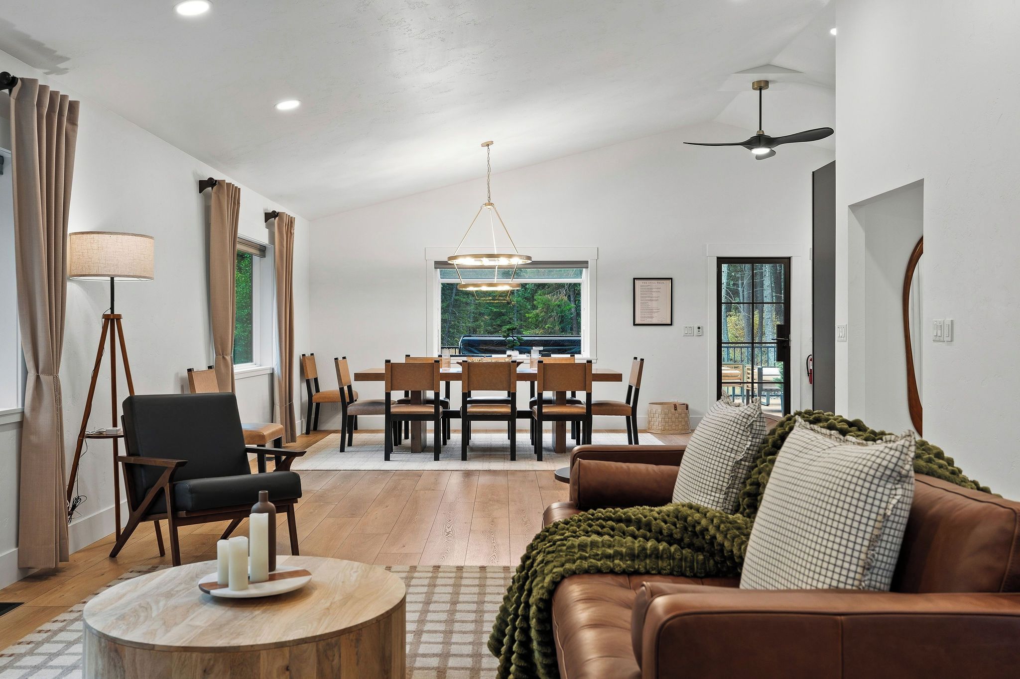 A spacious living room with a brown leather sofa, a dining table with chairs, a floor lamp, and a ceiling fan.