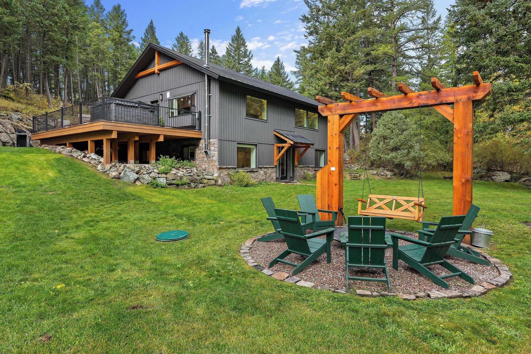 Une maison moderne à deux étages, avec des fondations en pierre, une terrasse en bois et un ensemble de jeux avec balançoire dans le jardin.