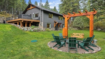 Une maison moderne à deux étages, avec des fondations en pierre, une terrasse en bois et un ensemble de jeux avec balançoire dans le jardin.