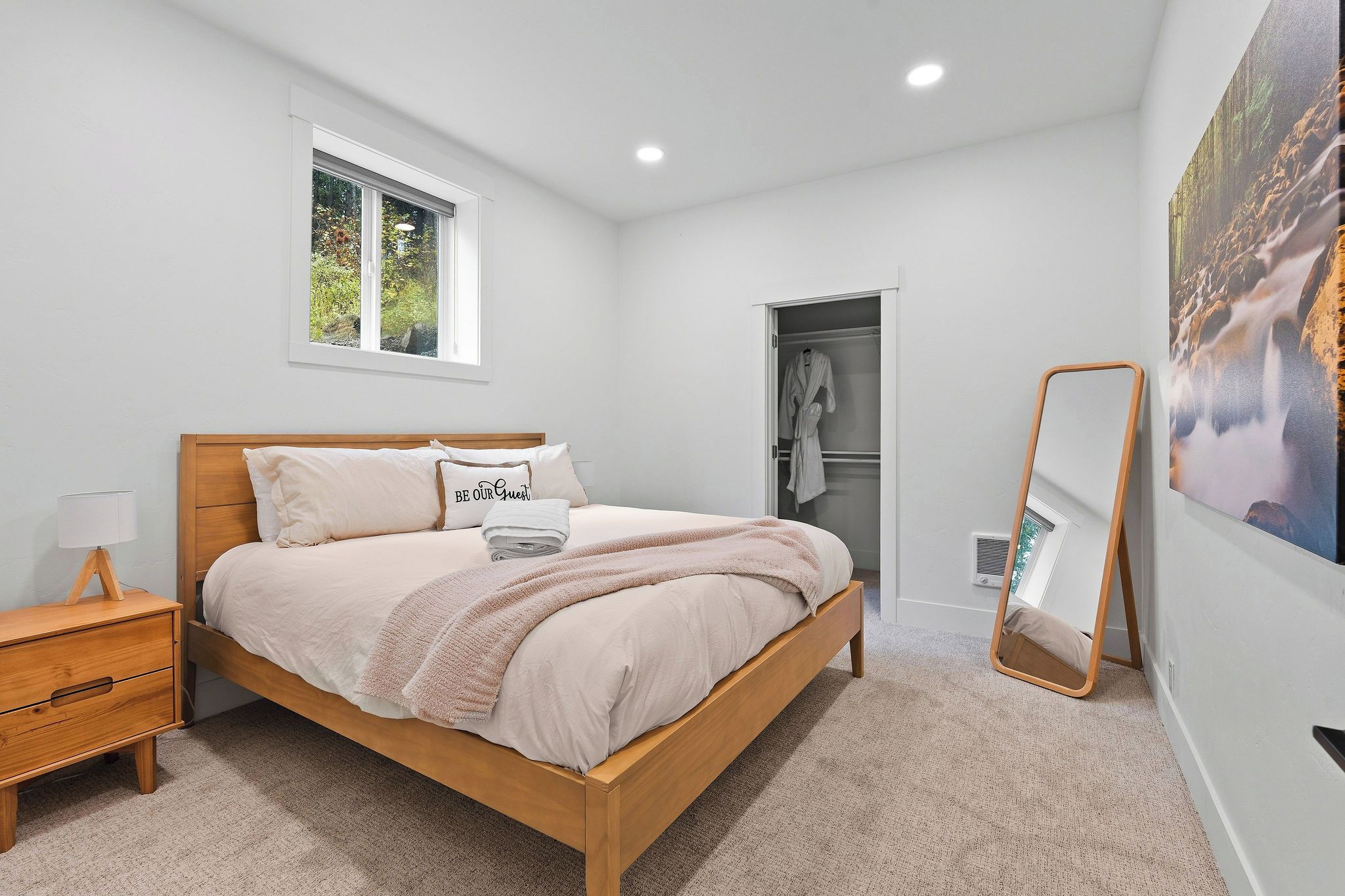 Une chambre à coucher avec un lit en bois, une table de chevet, une fenêtre, une armoire et un miroir.