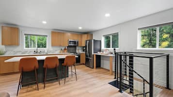 Eine moderne Küche mit Holzausstattung, einer zentralen Kochinsel mit Barhocker, einem Edelstahlkühlschrank und einer Treppe mit schwarzer Geländer.