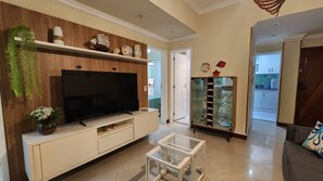 A living room with a flat-screen TV, wooden shelves, a glass cabinet with decorative items, and a sofa. - 3 Bedrooms in Copacabana - Near Arpoador (Rio de Janeiro)