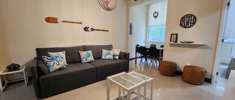 A living room with a dark sofa, a glass coffee table, and decorative pillows.