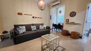 A living room with a dark sofa, a glass coffee table, and decorative pillows. - 3 Bedrooms in Copacabana - Near Arpoador (Rio de Janeiro)
