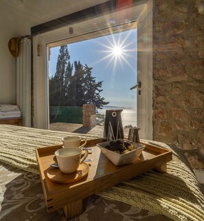Una habitación con una cama, una bandeja con tazas y un plato de comida, y vistas a árboles y un cuerpo de agua a través de una puerta de vidrio.