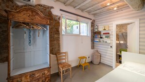 A room with a wooden wardrobe, a chair, a small stool, a window, and a door leading to another room. - Suite & Relax: The Exclusive Experience of Villa L'Altura (Cala Moresca)