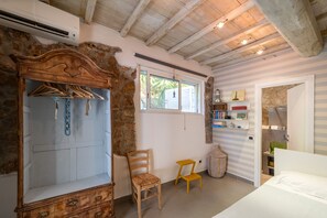 Una habitación con un armario de madera, una silla, un taburete pequeño, una ventana y una puerta que da a otra estancia.