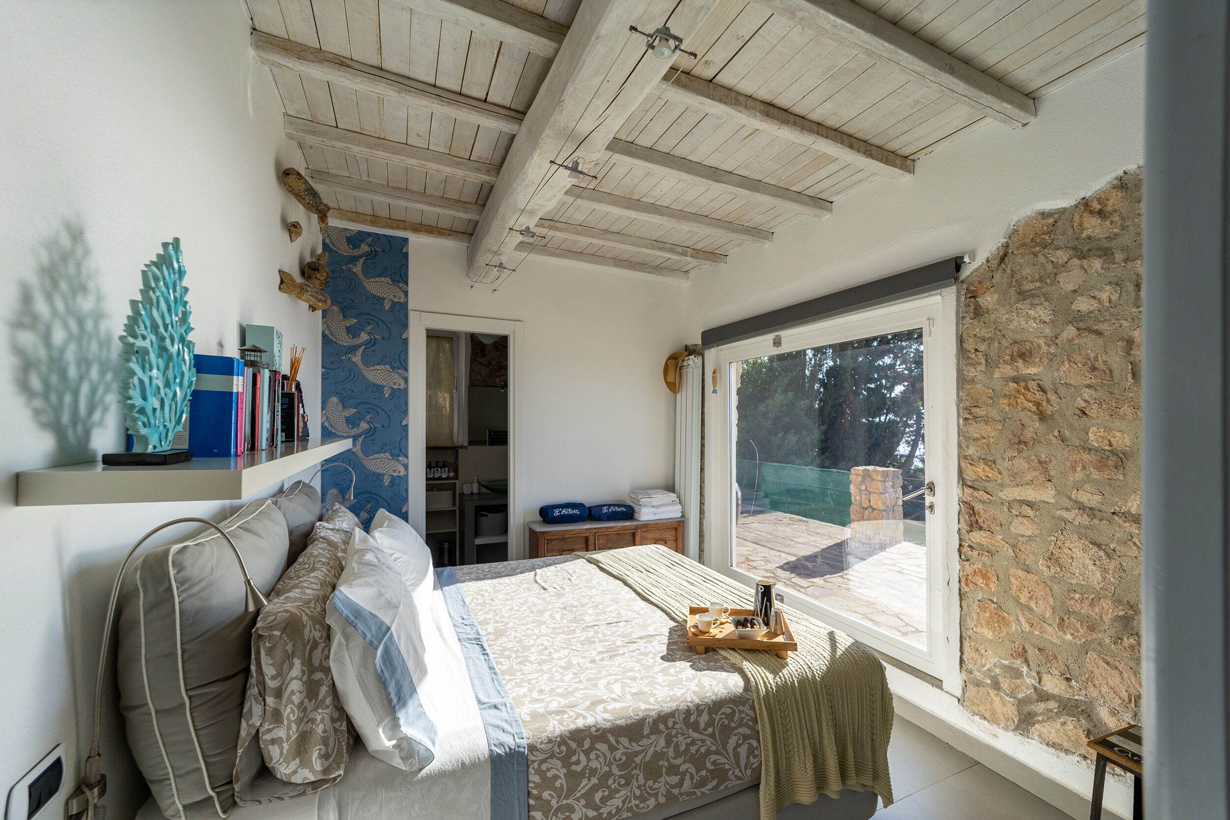 A bedroom with a bed, a window, a shelf with books, and a view of the outdoors.
