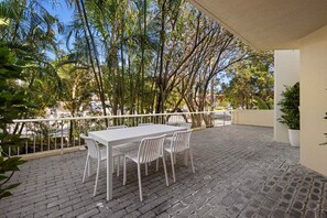 An outdoor patio with a white table and chairs, surrounded by a white railing, with trees and a clear sky in the background. - Burleigh Breeze 2‑Bed Beach Walk Retreat (Gold Coast)