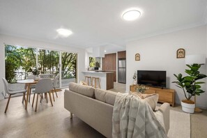 Una sala de estar moderna con un sofá, una mesa de comedor, sillas, un televisor y una zona de cocina.