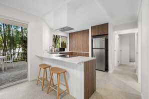 A modern kitchen with a large island, wooden cabinets, and a stainless steel refrigerator. - Burleigh Breeze 2‑Bed Beach Walk Retreat (Gold Coast)