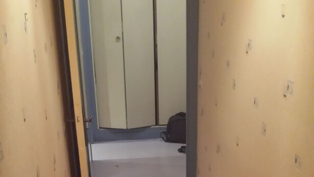 A hallway with a tiled floor, a door on the left, and a wall with small holes.