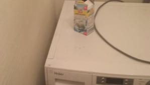 A front-loading washing machine with a control panel, a detergent dispenser, and a power cord.