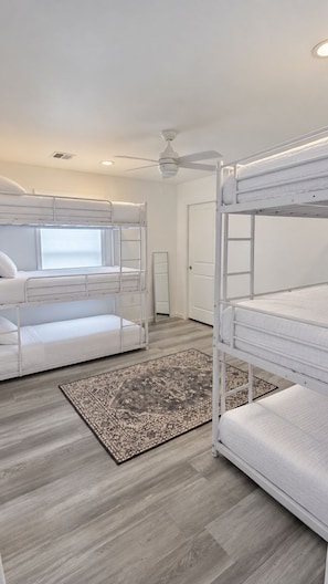 Ein Zimmer mit Etagenbetten, einem Deckenventilator, einem Fenster und einem gemusterten Teppich.