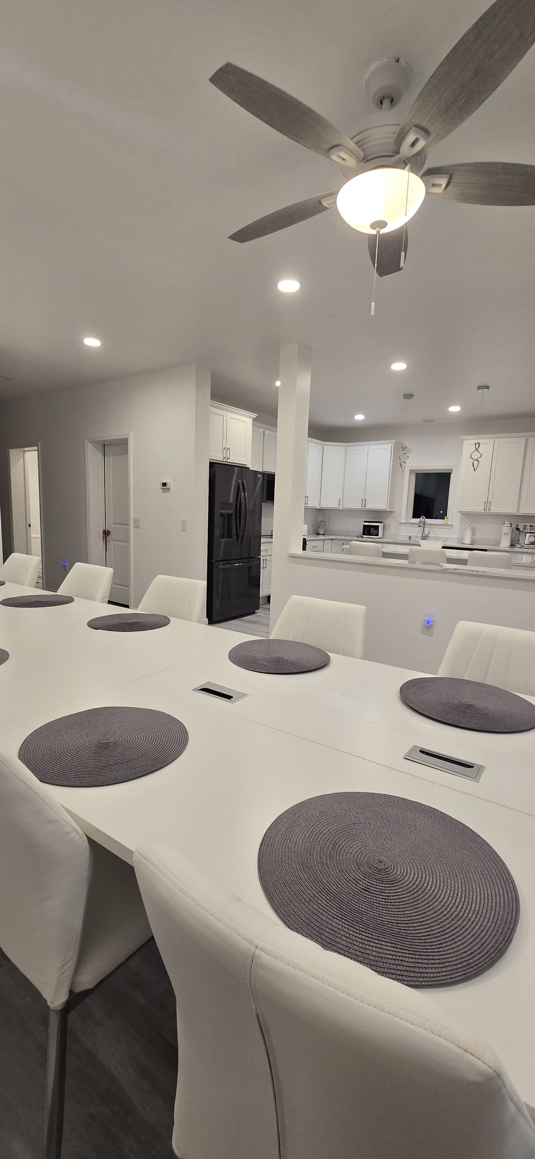 A modern kitchen with white cabinets, a black refrigerator, and a dining area with a long table and chairs.