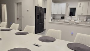 A modern kitchen with white cabinets, a black refrigerator, and a dining area with a long table and chairs. - Spacious 4-bedroom lake house in Shrewsbury MA.   (Shrewsbury)